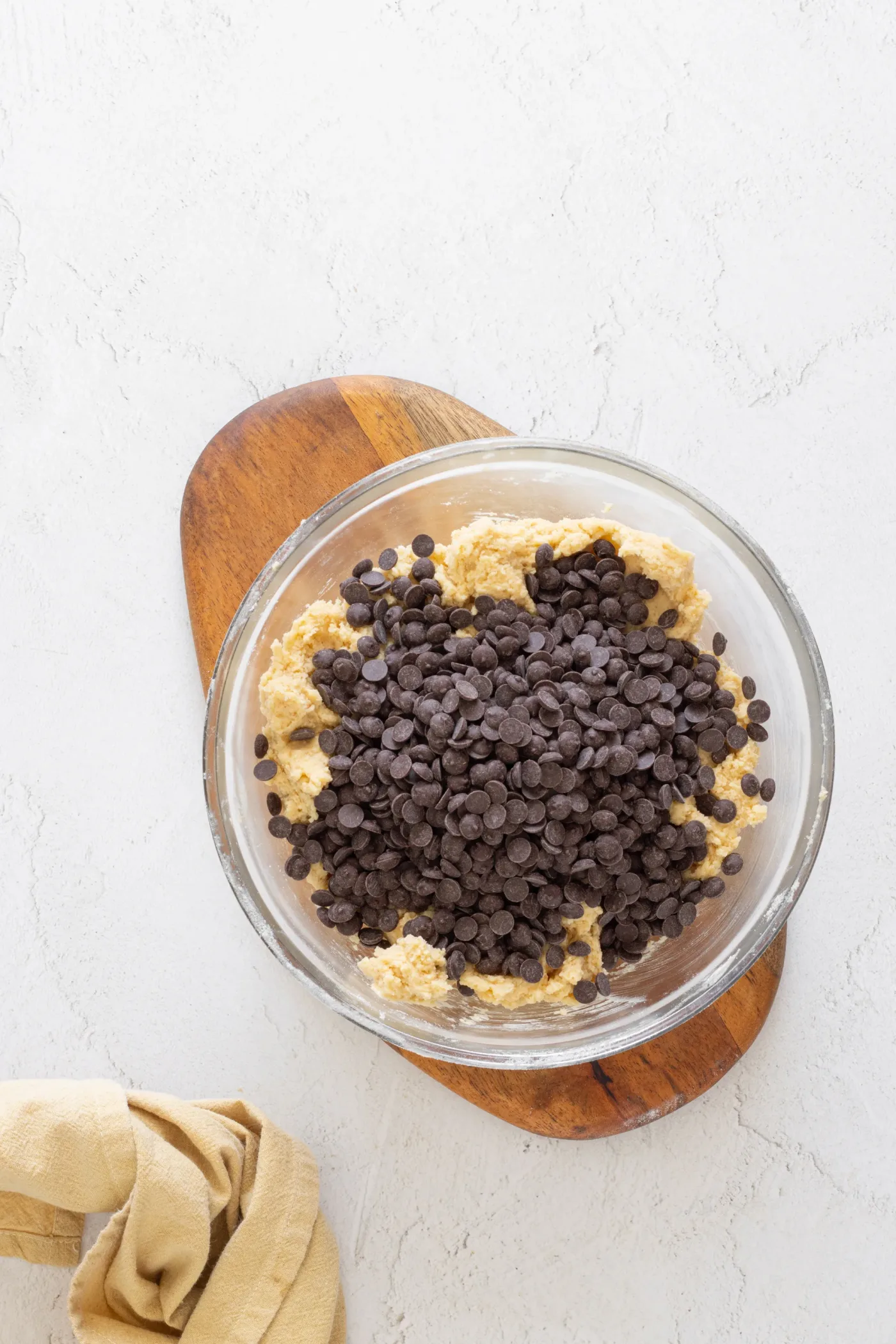 Chocolate chips piled over thick brown butter cookie dough in a glass bowl